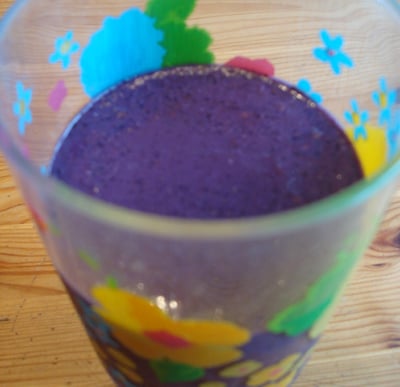 A glass with a blueberry green smoothie.