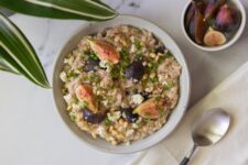 A white bowl filled with savory oatmeal with figs and feta and a napkin with a spoon with a small bowl filled with figs.