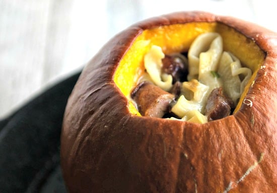 A closeup of a roasted pumpkin that is stuffed with pasta.