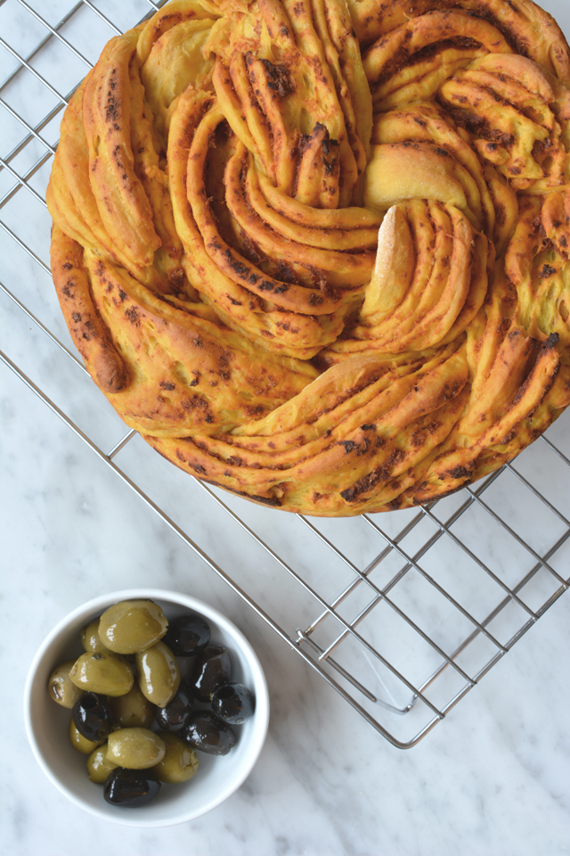 Sweet Potato and Sun Dried Tomato Braided Bread on a cooling rack with a bowl of green olives.