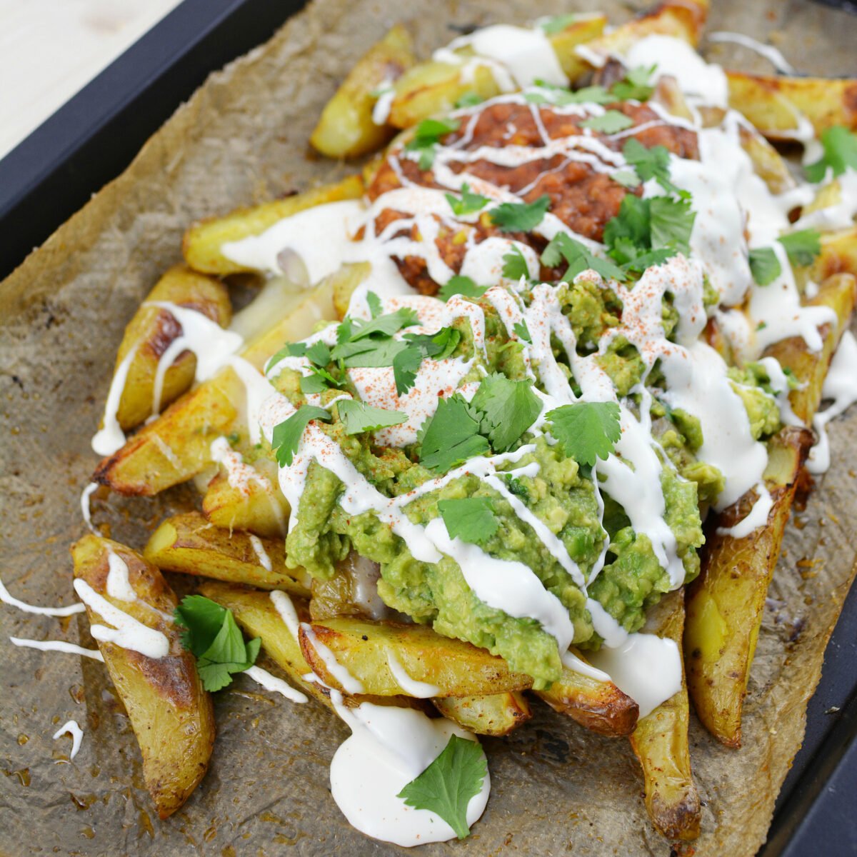 cropped image of a potato wedges nachos topped with guacamole, salsa and sour cream