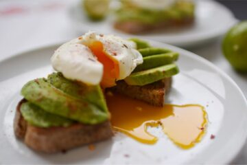 Avocado and poached egg on toast with the yolk spilling out onto a white plate.