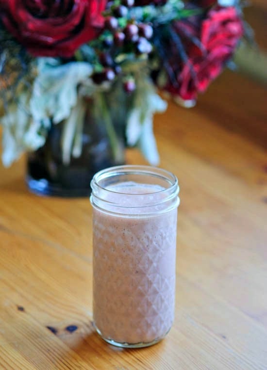 A glass filled with a strawberry smoothie with flowers in the background. 