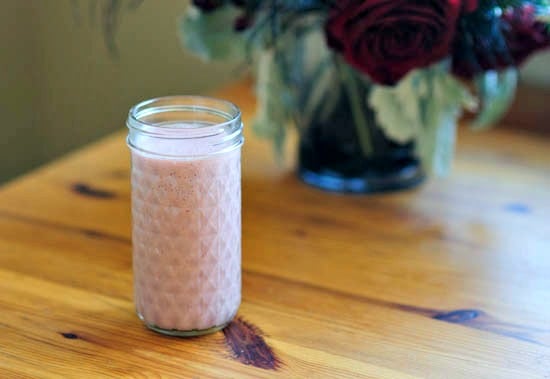 A jar of strawberry date smoothie on a wooden table.