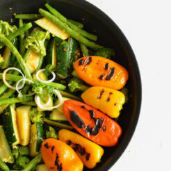 half view image of a bowl containing stir fried zucchini, broccoli, snap peas, with roasted bell peppers,