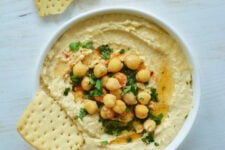 hummus recipe in a bowl topped with checakpeas and a piece of cracker