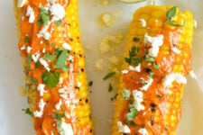 cropped image of 2 Grilled Corns Topped with Lime Butter and Crumble Feta Cheese, and Fresh chopped Coriander