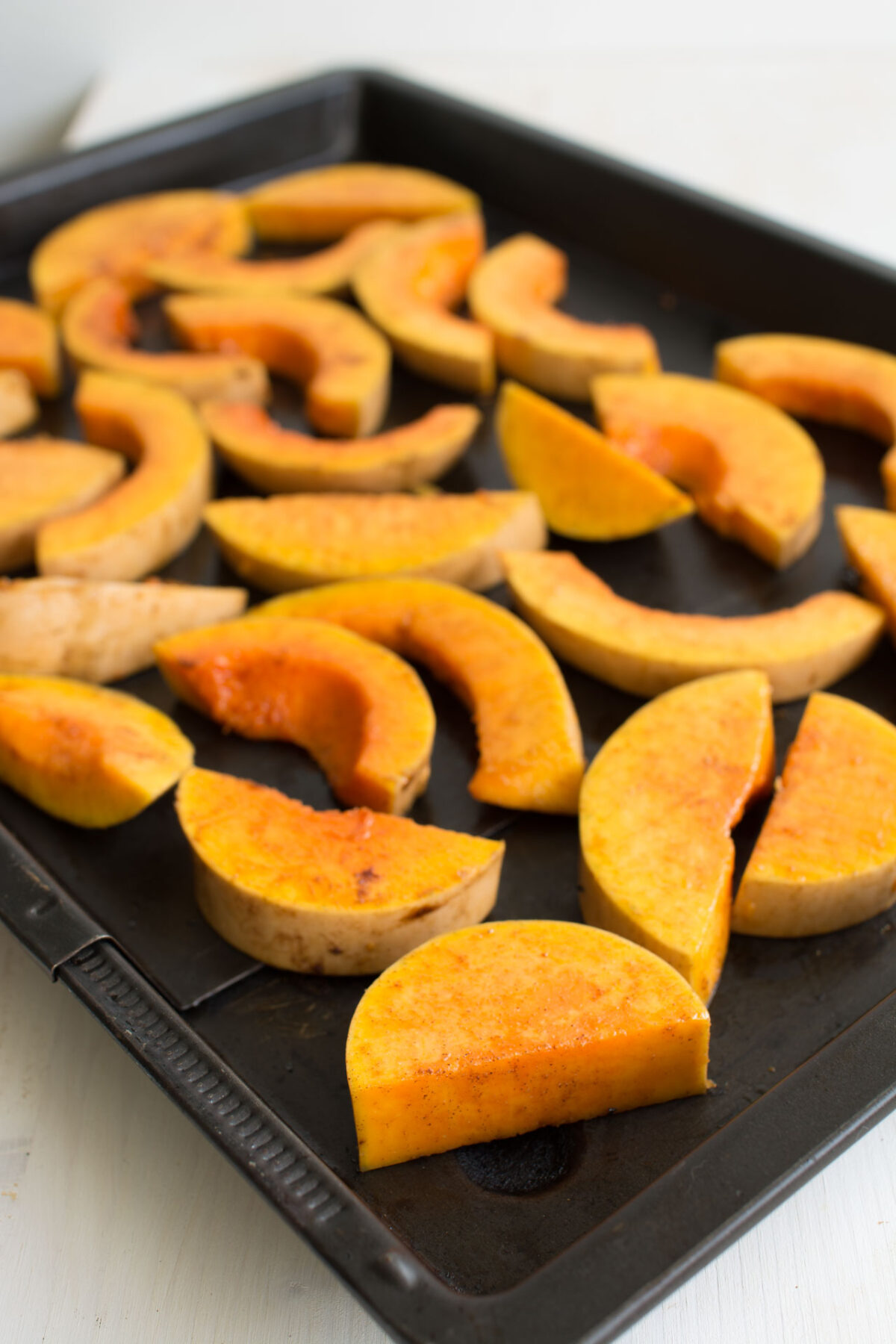an image of sliced raw butternut squash spread evenly in a baking tray