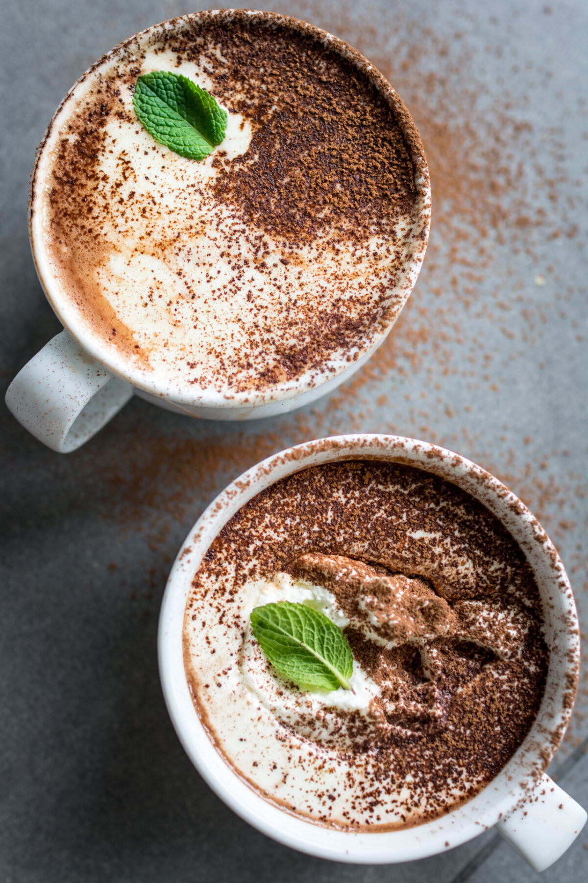 Top view of two cups of dairy-free peppermint hot chocolate with cocoa sprinkled on top and garnished with a mint leaf.