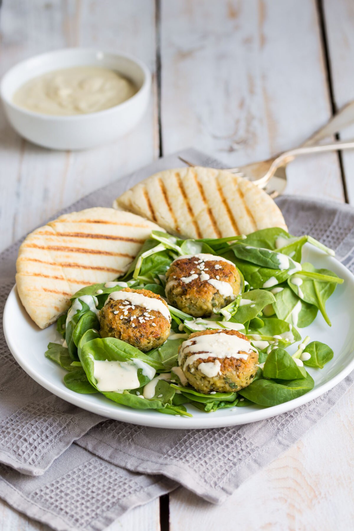 close up image of homemade falafel in a plate topped with a creamy, and tahini dressing