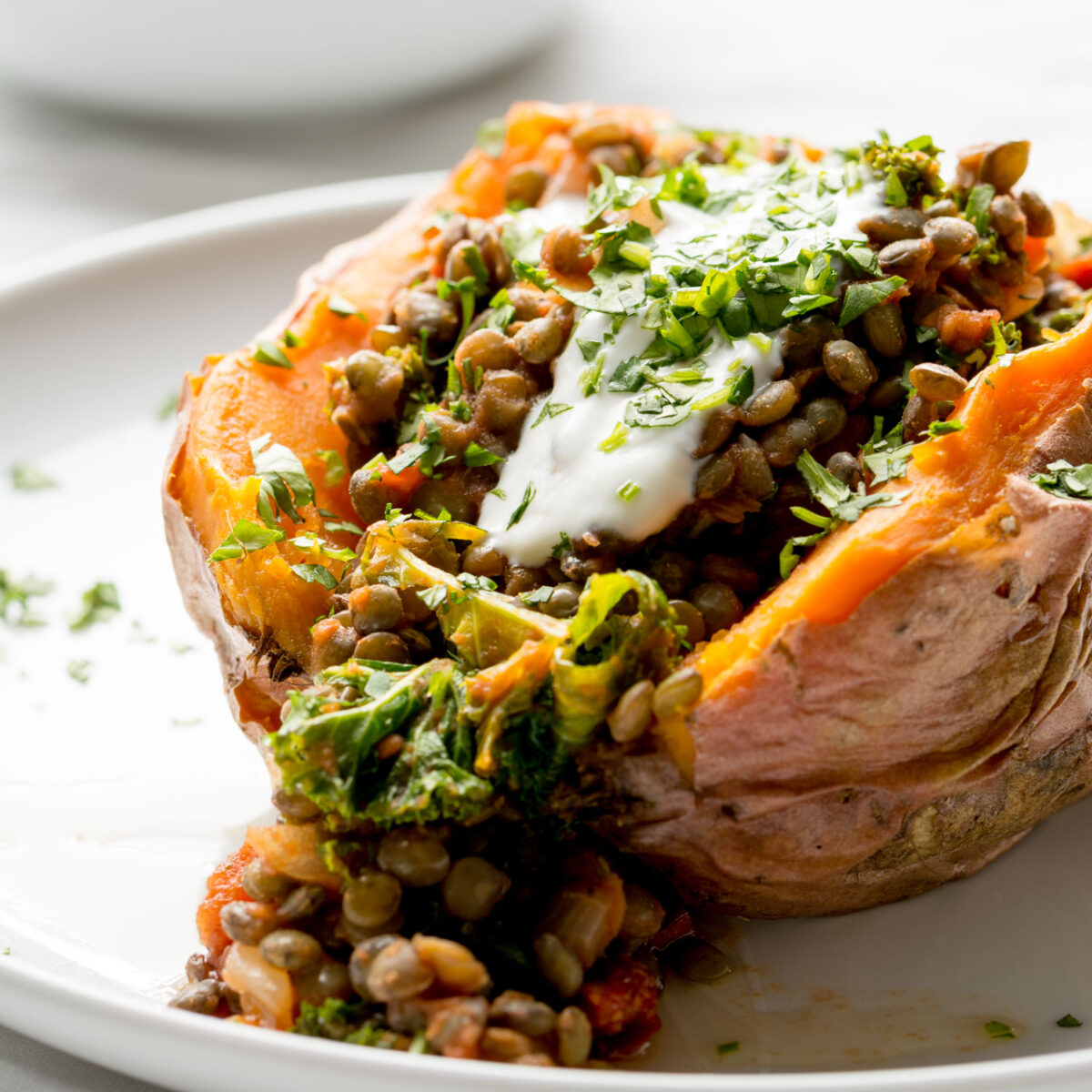 Sweet Potato stuffed with lentils, kale and sun dried tomatoes on a white plate with some contents spilling out.