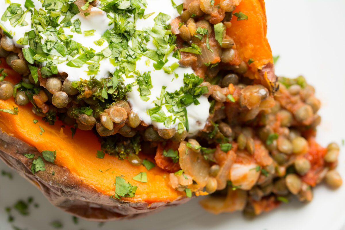 Sweet Potato stuffed with lentils, kale and sun dried tomatoes and topped with yogurt and cilantro close up.