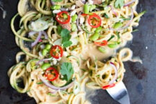 close up view image of a thai zucchini noodle salad top with edamame beans, onions, chopped red chili, peanuts, spring onions, parsley,