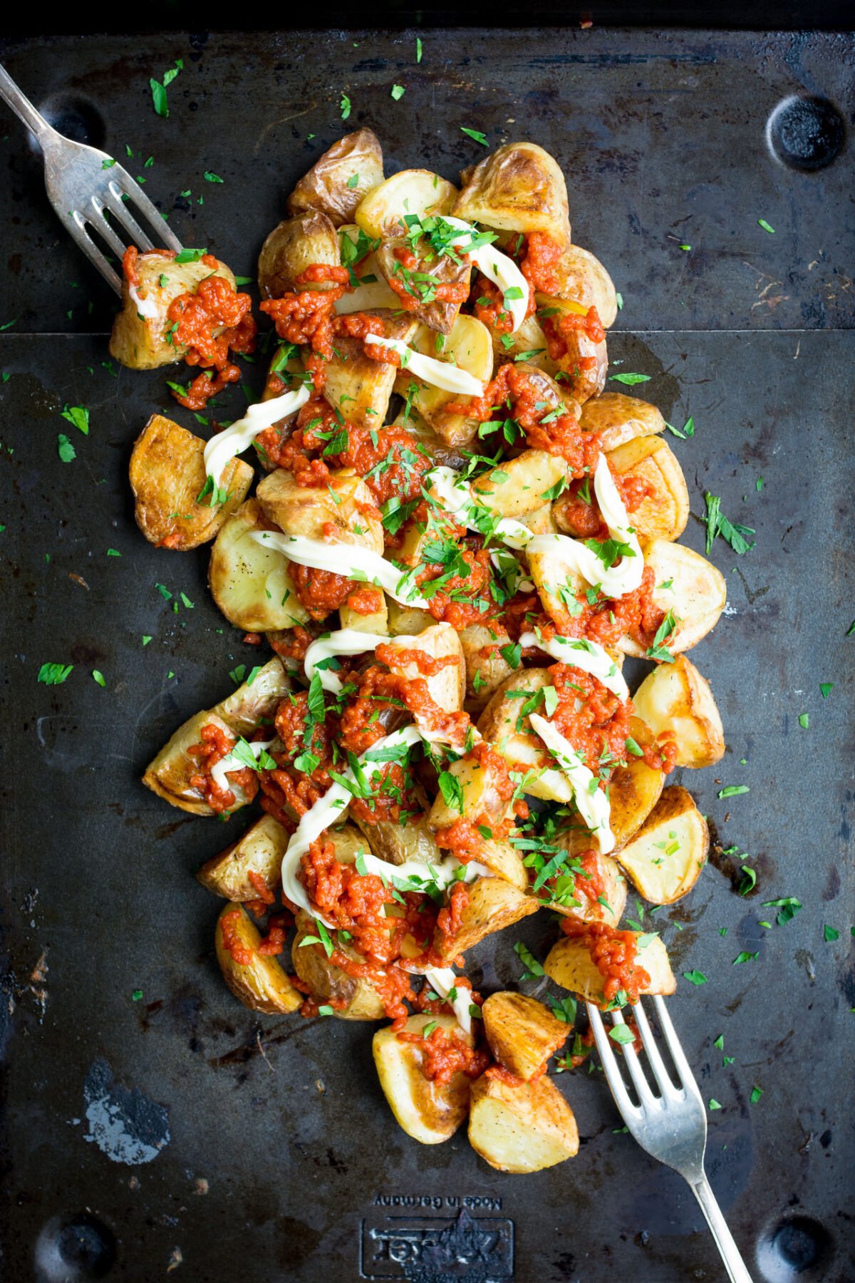 Seasoned patatas bravas on a griddle top covered in tomato sauce with a fork.