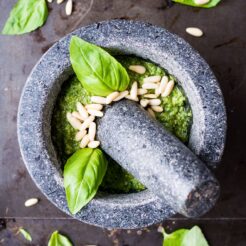 top down image of a stone mortar containing smooth mixture of pesto with basil leaves and pinenuts