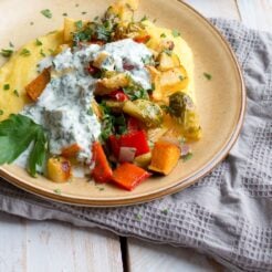 a cropped image of a colorful roasted vegetables, creamy polenta, and zesty herby yogurt sauce on a plate