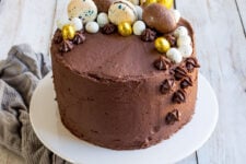close up image of a moist vanilla layer cake covered in chocolate orange frosting topped with chocolate eggs and macarons