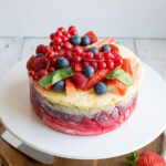 close up image of a delicious and colorful yogurt layer cake topped with strawberries, rapsberries, and blueberries
