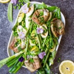 top down cropped photo of a serving dish containing grilled spring vegetables including french green beans, spring onions, sugar snap peas, asparagus, leeks, and artichokes, glisten with a homemade lemon parsley butter