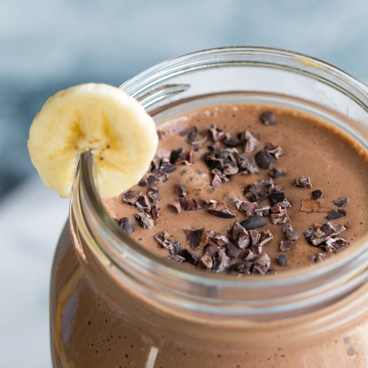 A jar with a peanut butter chocolate smoothie with a slice of banana.