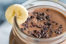 A jar with a peanut butter chocolate smoothie with a slice of banana.