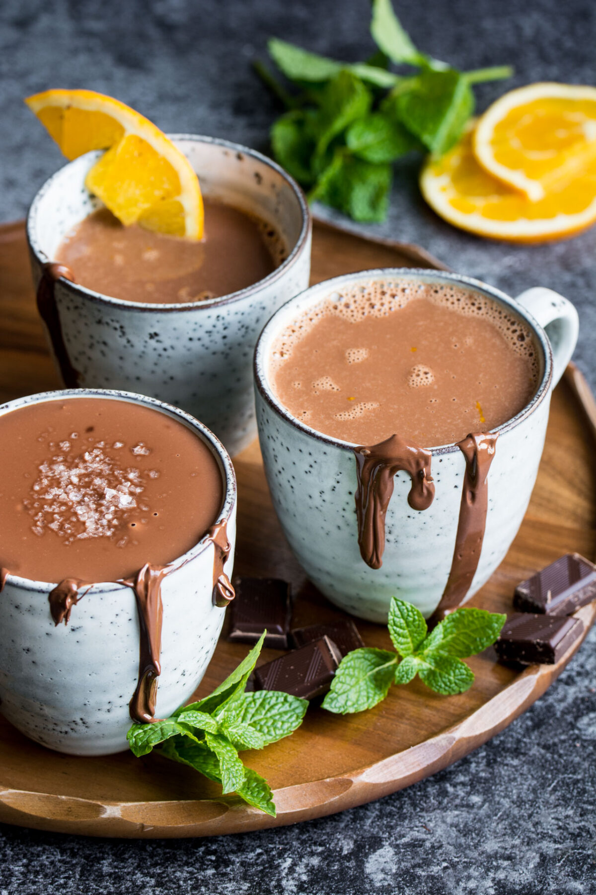 Three cups of thick Italian hot chocolate with chocolate dripping down the sides and topped with flaked sea salt. 