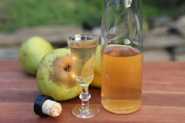 Spiced pear liqueur on a wooden cutting board with Bartlett pears in the background.