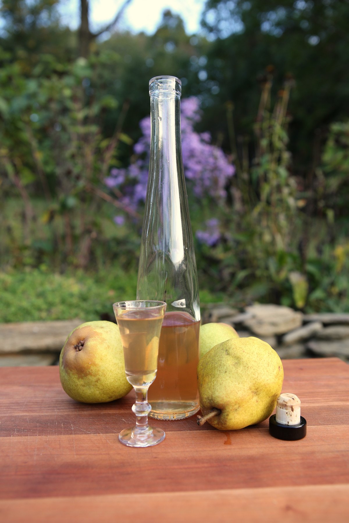 Spiced pear liqueur on a wooden cutting board with Bartlett pears in the background (vertical orientation).