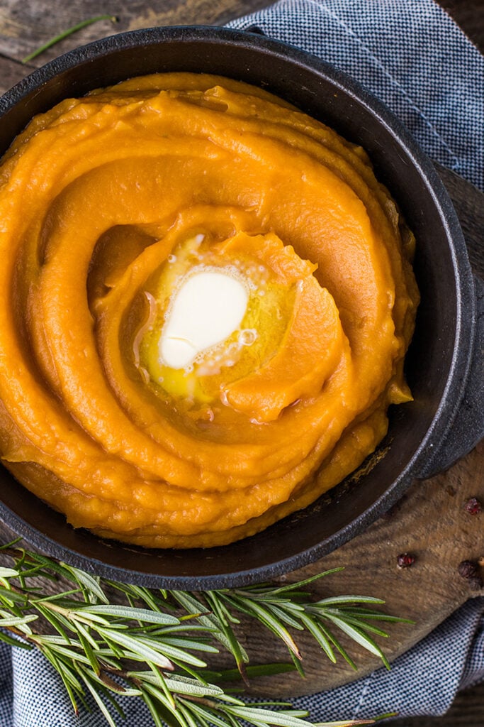 Healthy mashed sweet potato with rosemary in a cast iron saucepan on a table.