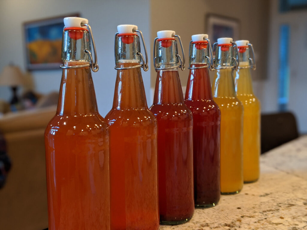 6 bottles of homemade kombucha in flip-top bottles on a kitchen counter.