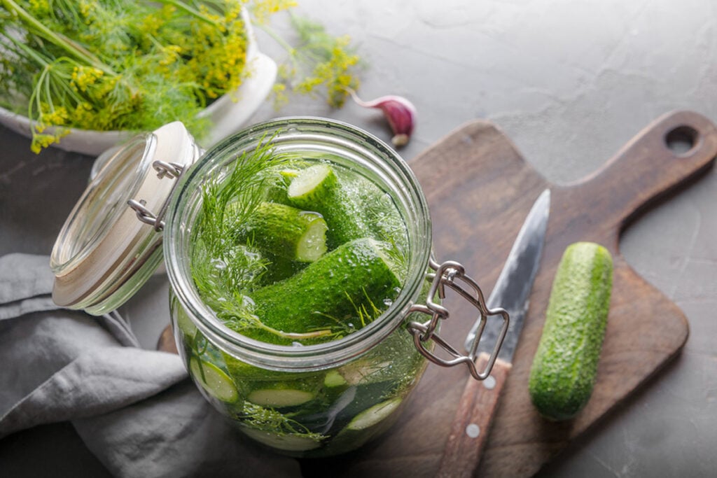 Pickling and fermentation cucumber in glass jar with dill and garlic on dark grey concrete table.