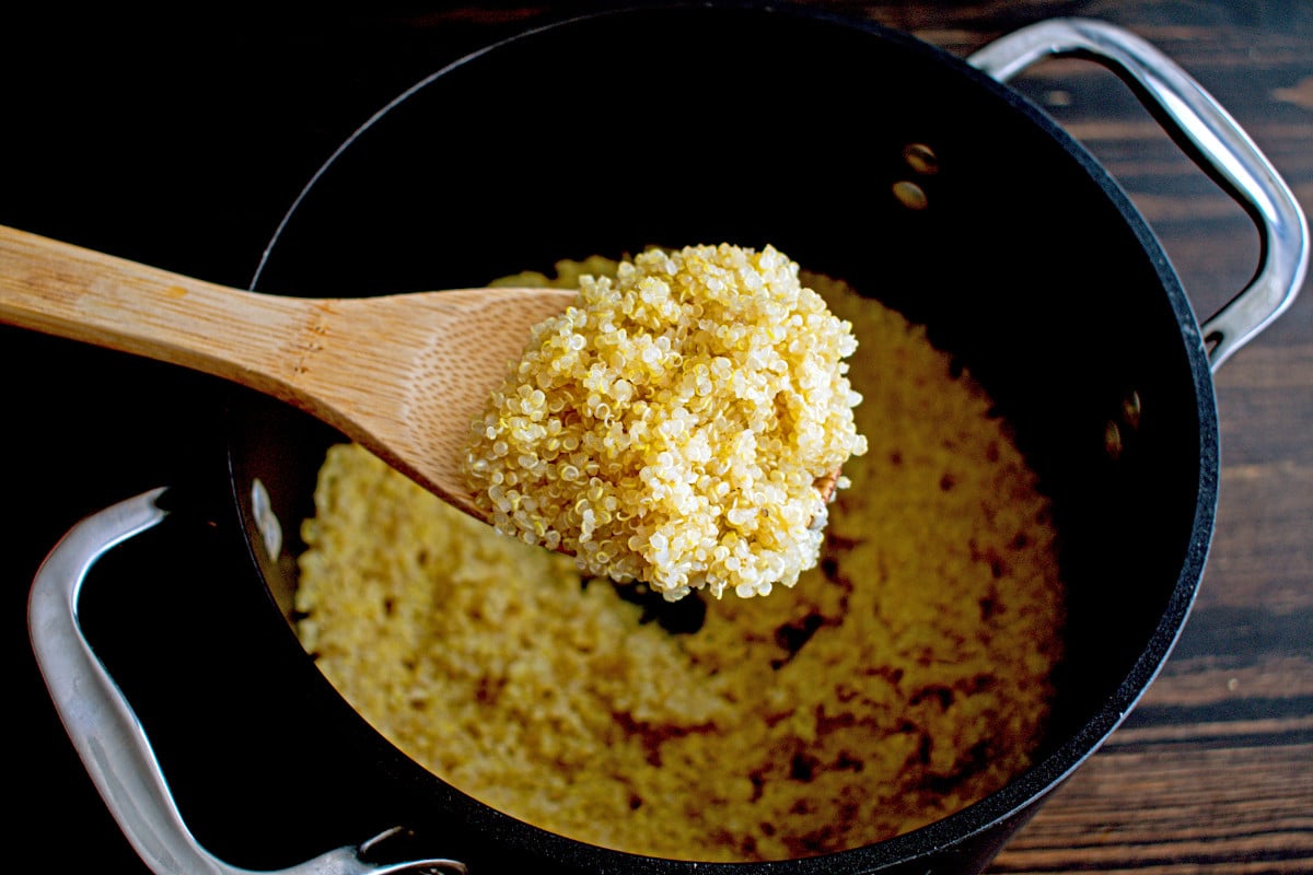 Cooked quinoa in a wooden spoon over a saucepan.