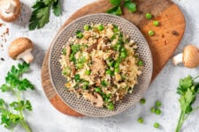 Couscous with fried mushrooms, onions, green peas, and parsley in a plate on a grey background top view.