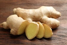 Fresh ginger root with slices on wooden table.