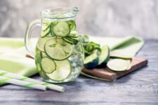 A glass pitcher filled with cucumber water, flavored with lime and mint.