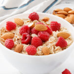 Oatmeal with almonds and raspberries in a white bowl - square image.