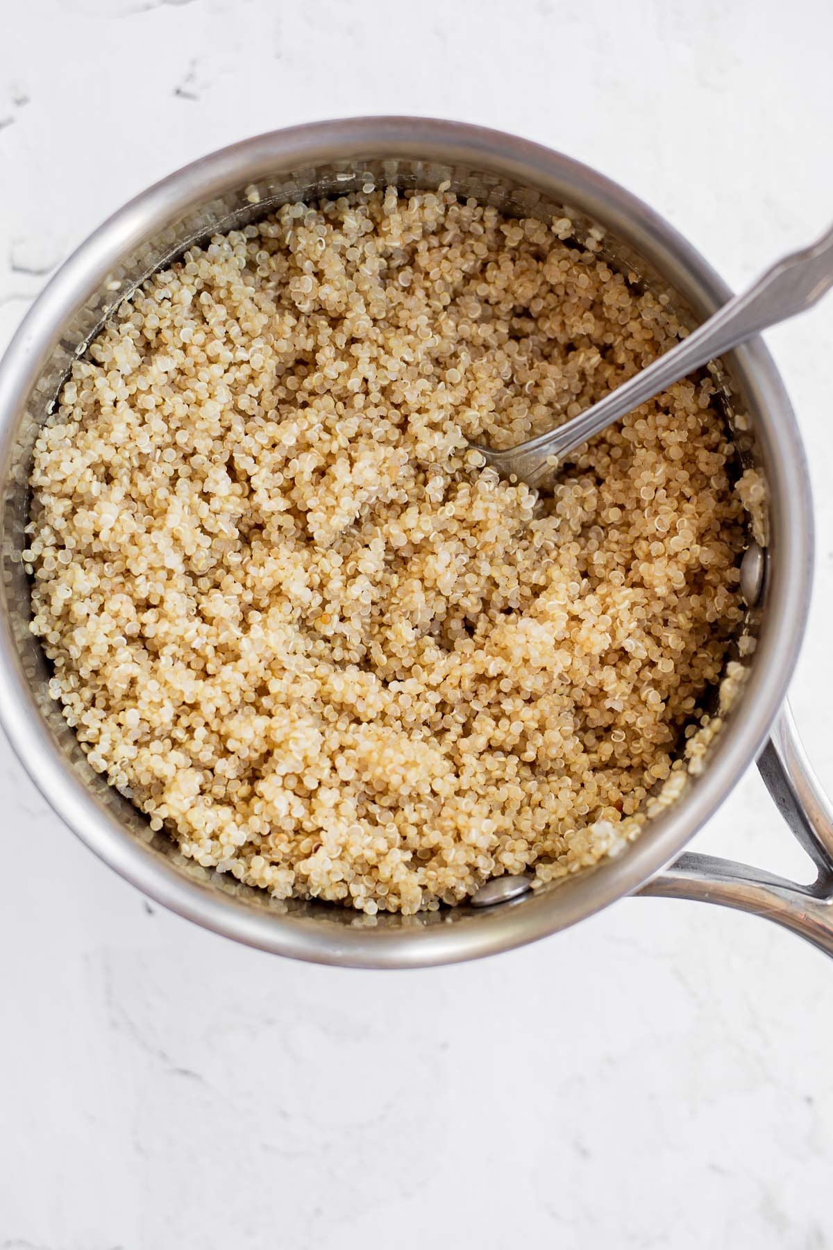 Cooked quinoa in a saucepan with a fork.