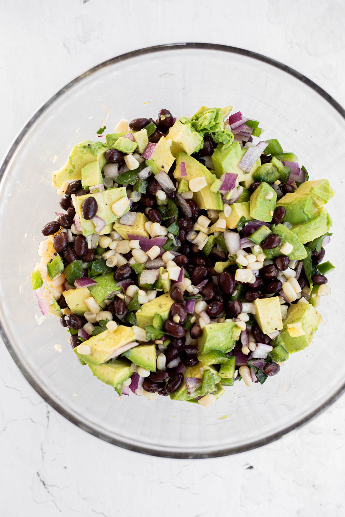 Black beans, corn, avocado, green pepper, and red onions in a glass bowl.