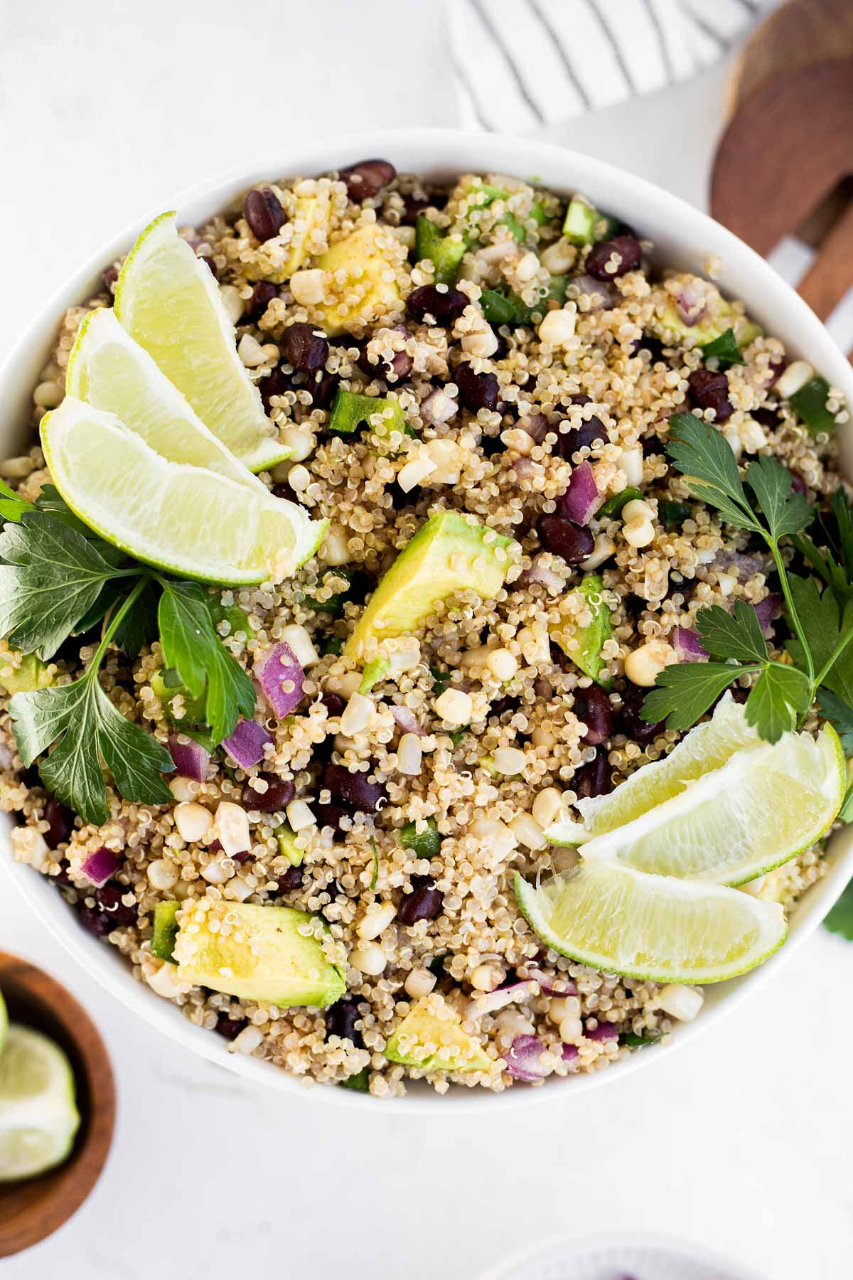 Vertical image of quinoa salad with black beans and corn garnished with lime wedges and cilantro.