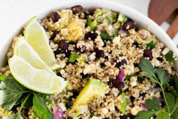 Close-up view of quinoa salad with black beans and corn garnished with lime wedges and cilantro.