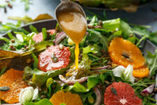 Vinaigrette dressing pouring from a spoon onto a fresh fruit salad with mixed greens.