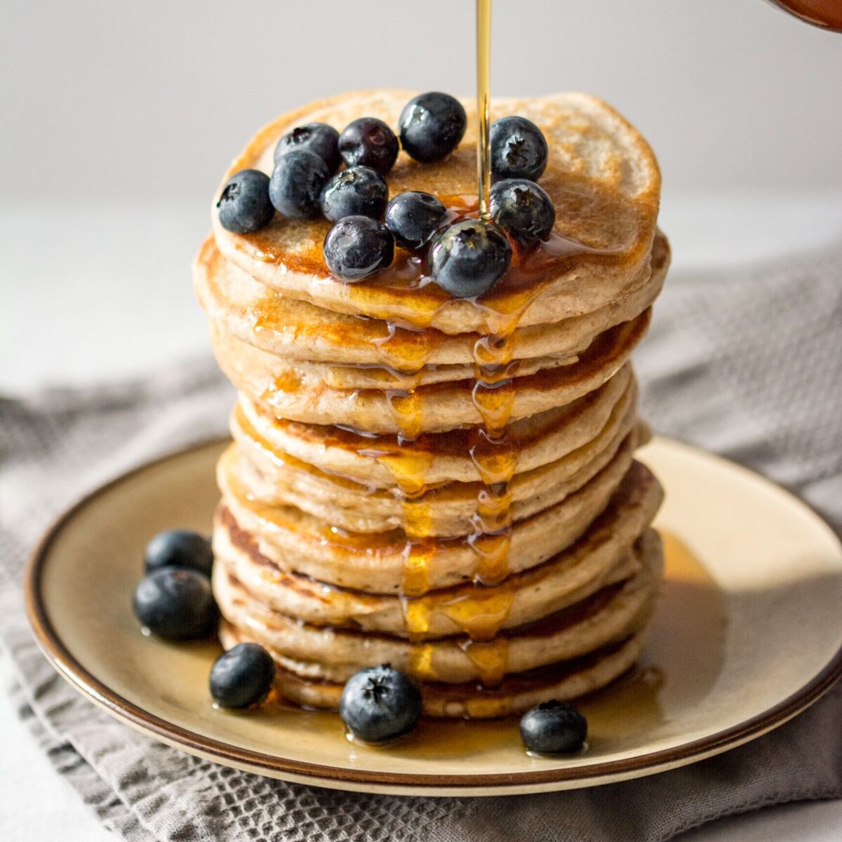 A stack of banana pancakes with maple syrup and blueberries.