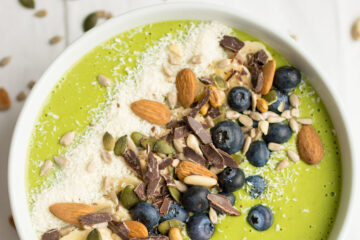 Green Smoothie bowl topped with almonds, blueberries, seeds and chocolate.