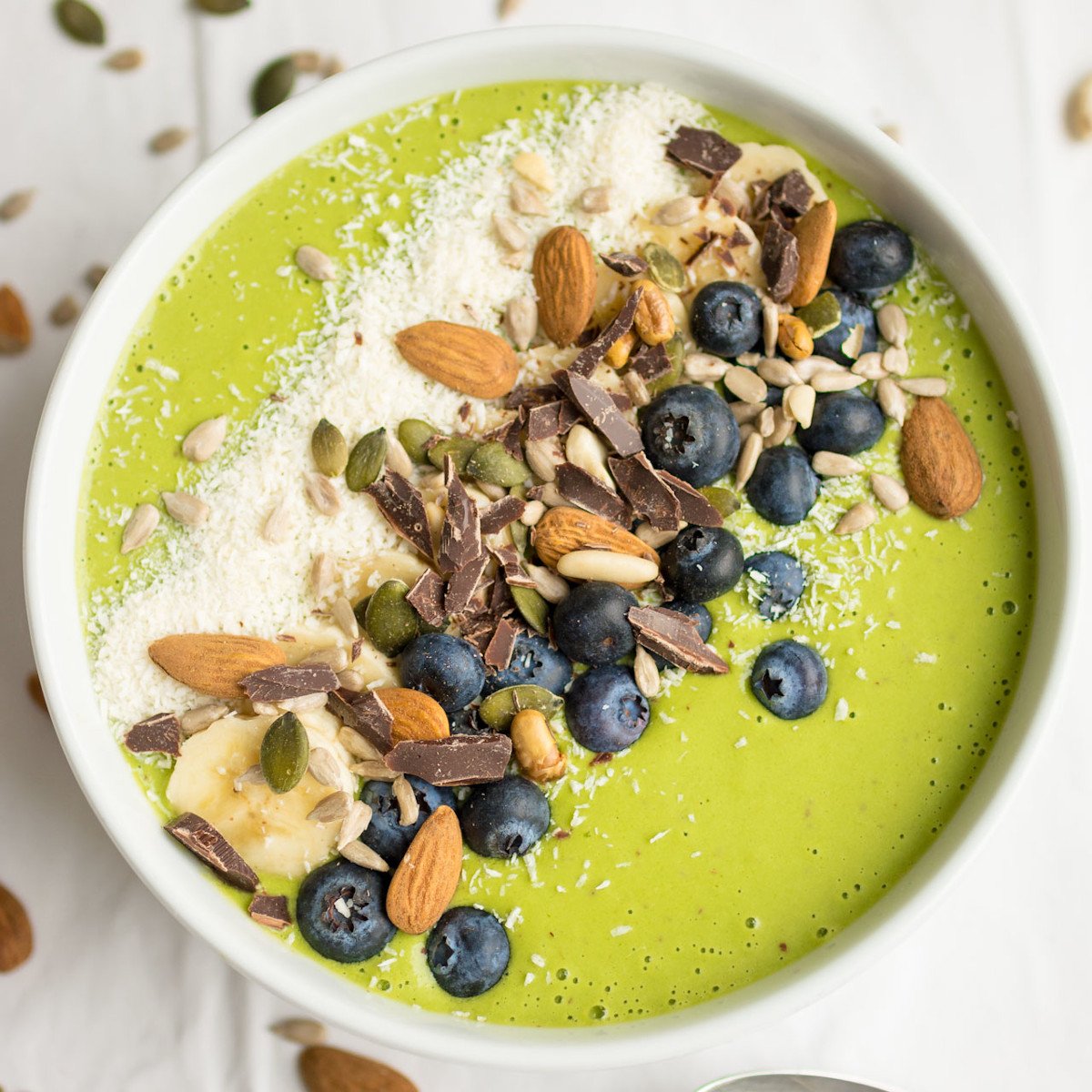 Green Smoothie bowl topped with almonds, blueberries, seeds and chocolate.