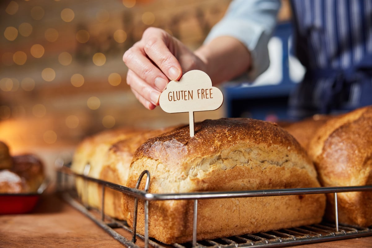 A hand sticking a "Gluten" label into a loaf of fresh-baked bread.