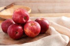 Red apples on a wooden table surrounded by burlap with a wooden bowl and knife int he background.