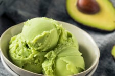 Avocado ice cream in a white bowl with an avocado blurred in the background.