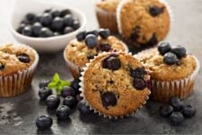 Blueberry muffins on a dark surface with more muffins and blueberries in the background.