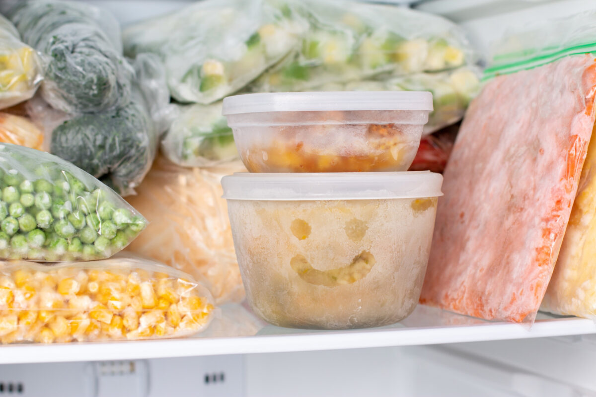 Plastic bags full of frozen vegetables in a freezer with a plastic container with a happy face on it.
