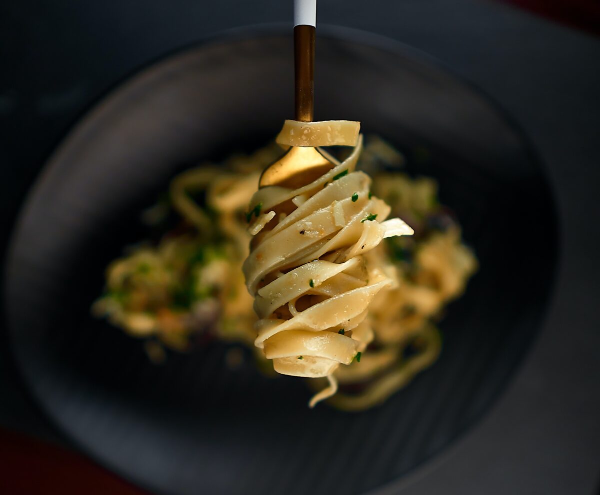 Italian fettucine pasta wrapped around a fork over a black bowl.